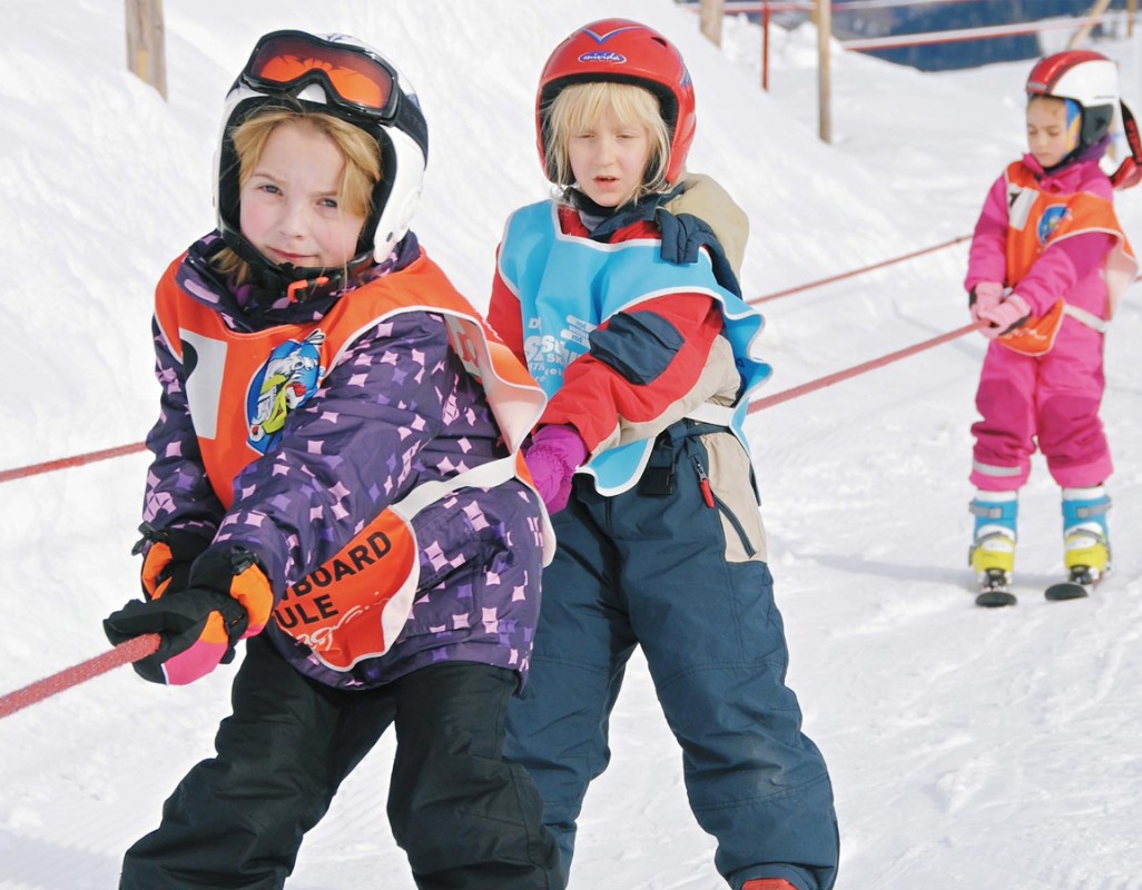 Kinderen in skikleding rijden op een skilift de helling op.
