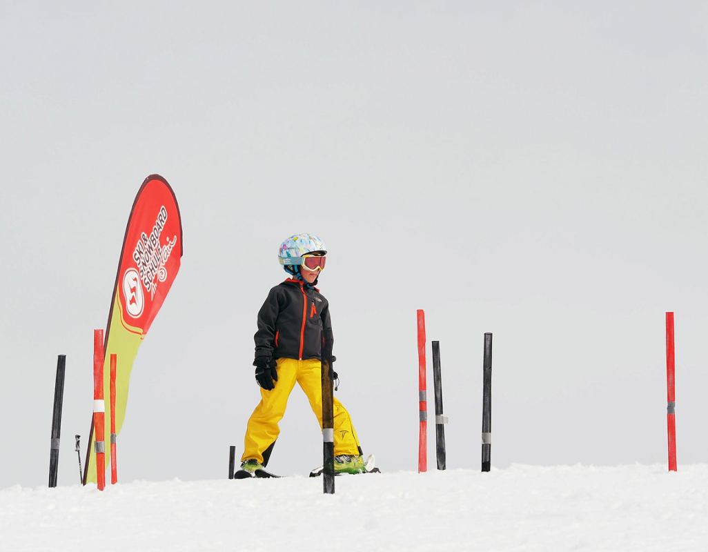 Kind in kleurrijke skikleding staat op een besneeuwde piste naast rode palen