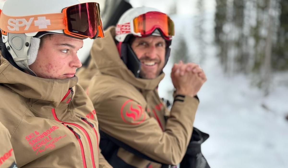Twee personen in skikleding zitten naast elkaar in de sneeuw.