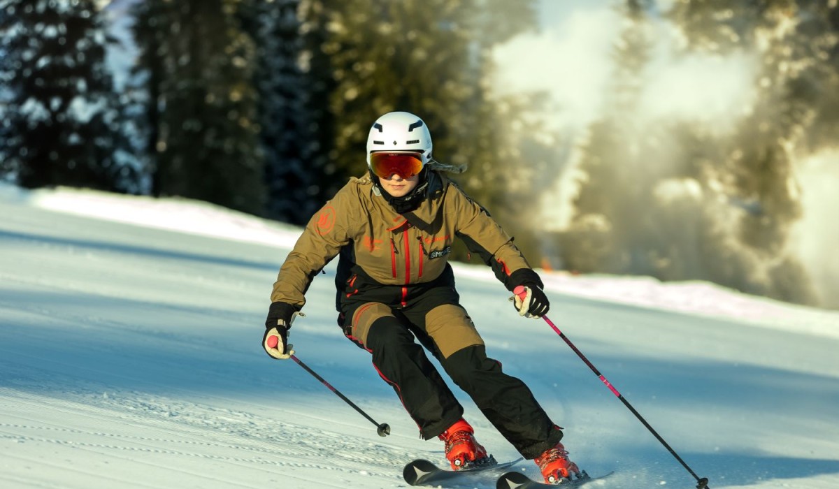 Skiër in bruine jas skiet op een besneeuwde piste met een zonnige achtergrond