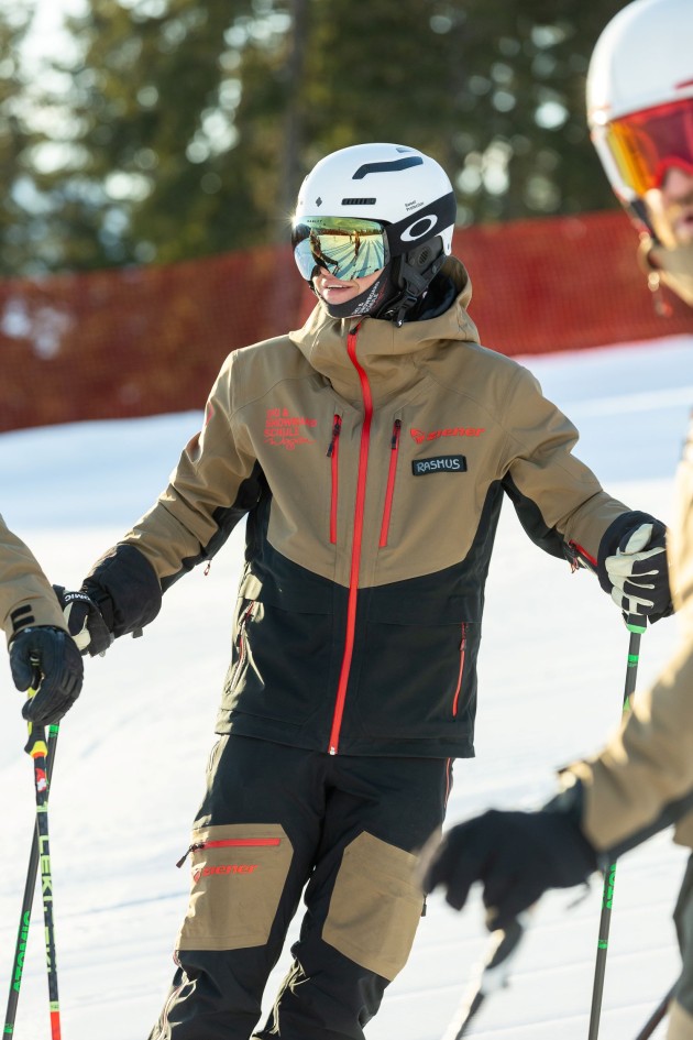 Skifahrer in brauner Jacke mit Helm auf der Piste