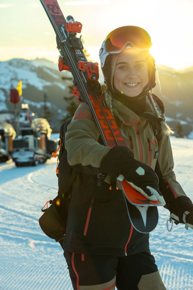 Skifahrerin bei Sonnenaufgang auf der Piste mit Skiern auf der Schulter