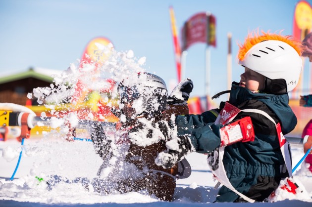 Zwei Kinder spielen lachend im Schnee und werfen Schneebälle