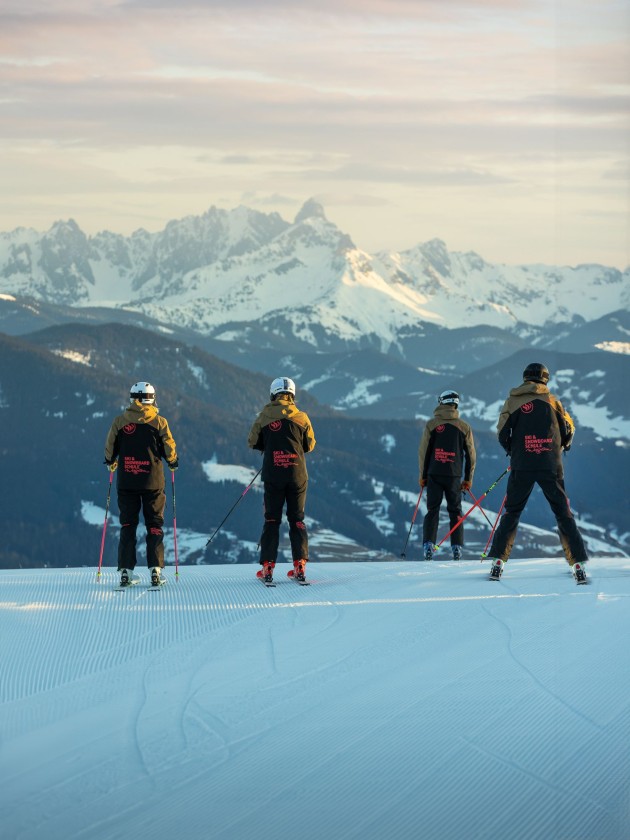 Skifahrer in schwarzer Kleidung stehen auf einer Piste mit Bergblick im Hintergrund